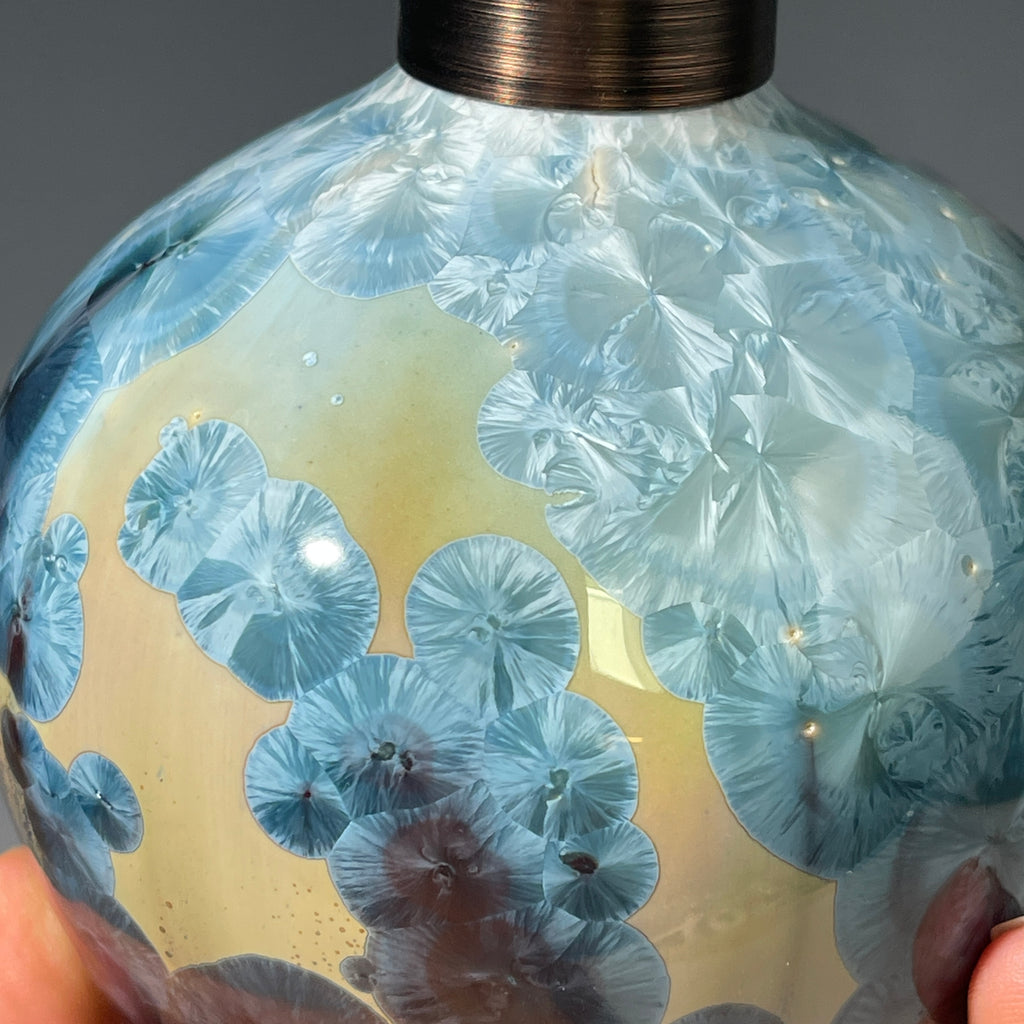 A close-up of a decorative ceramic soap pump featuring a light blue teal and maroon charcoal crystalline glaze