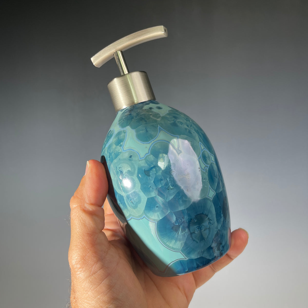 close up of a unique art soap dispenser by Hong Rubinstein in an ocean hued sparkling refractive  macro crystalline glaze