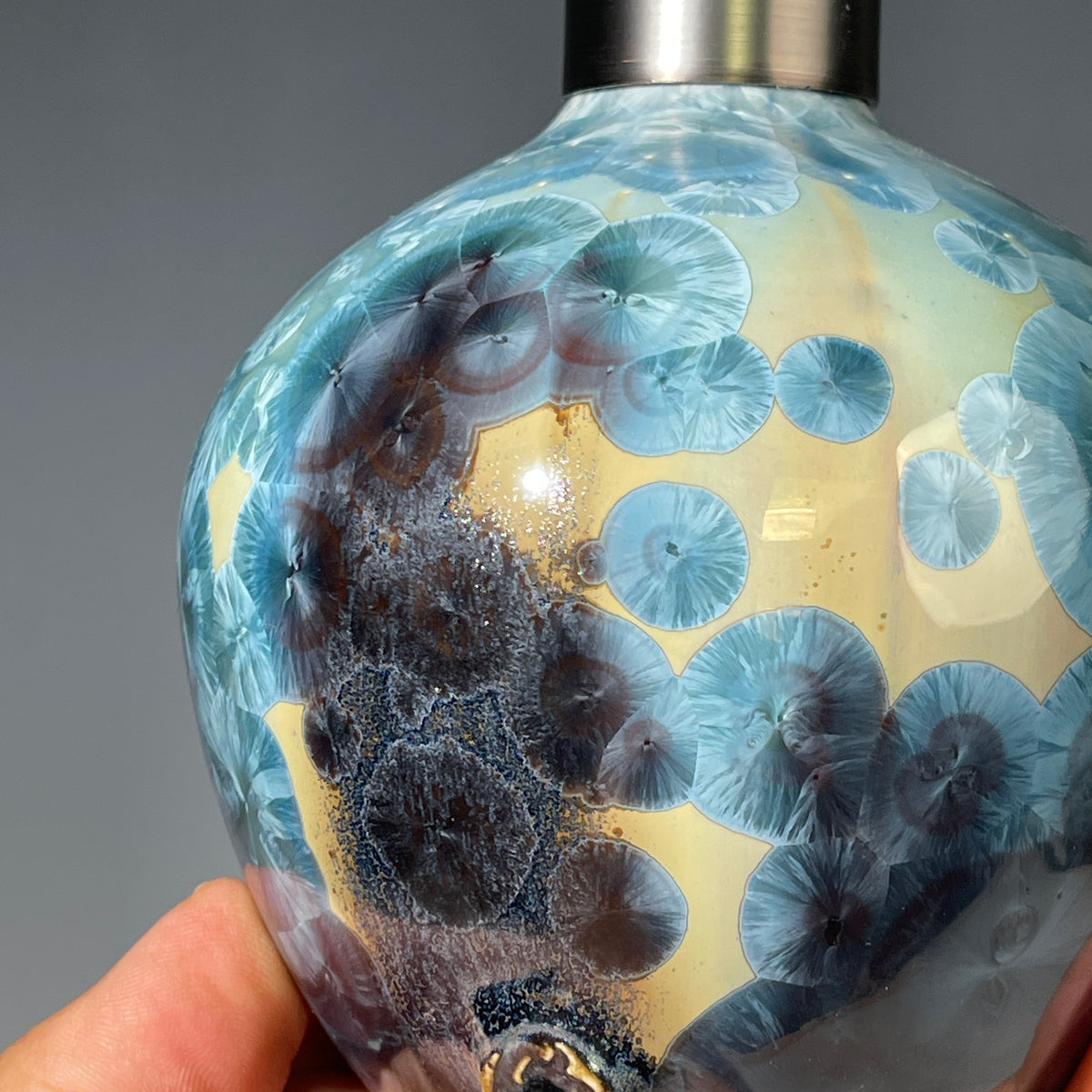 A close-up of a decorative ceramic soap pump featuring a light blue teal and maroon charcoal crystalline glaze