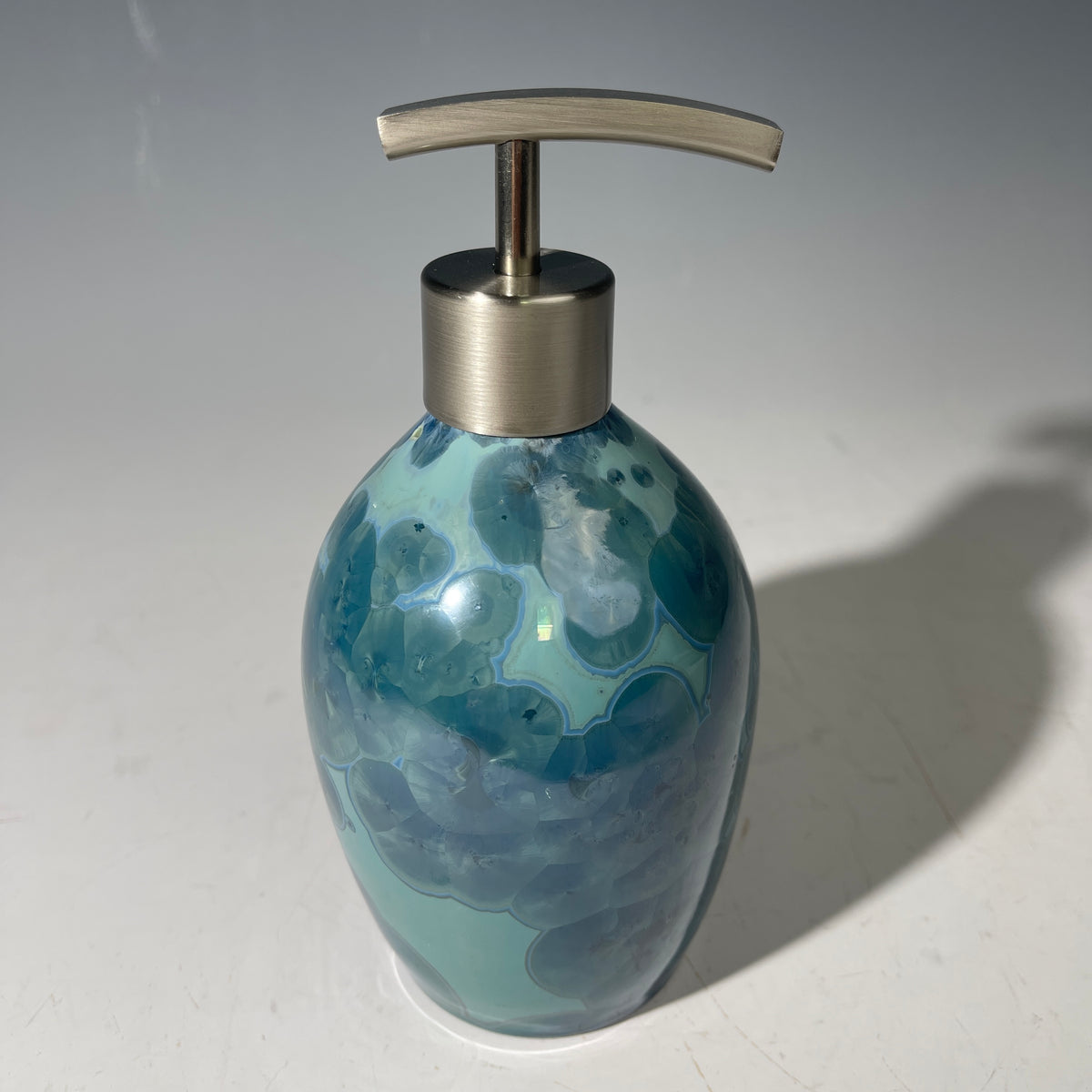 close up of a unique art soap dispenser by Hong Rubinstein in an ocean hued sparkling refractive  macro crystalline glaze