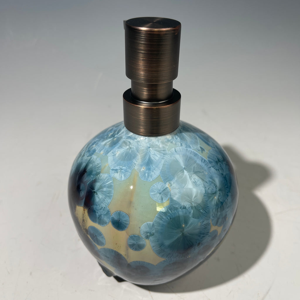 A close-up of a decorative ceramic soap pump featuring a light blue teal and maroon charcoal crystalline glaze