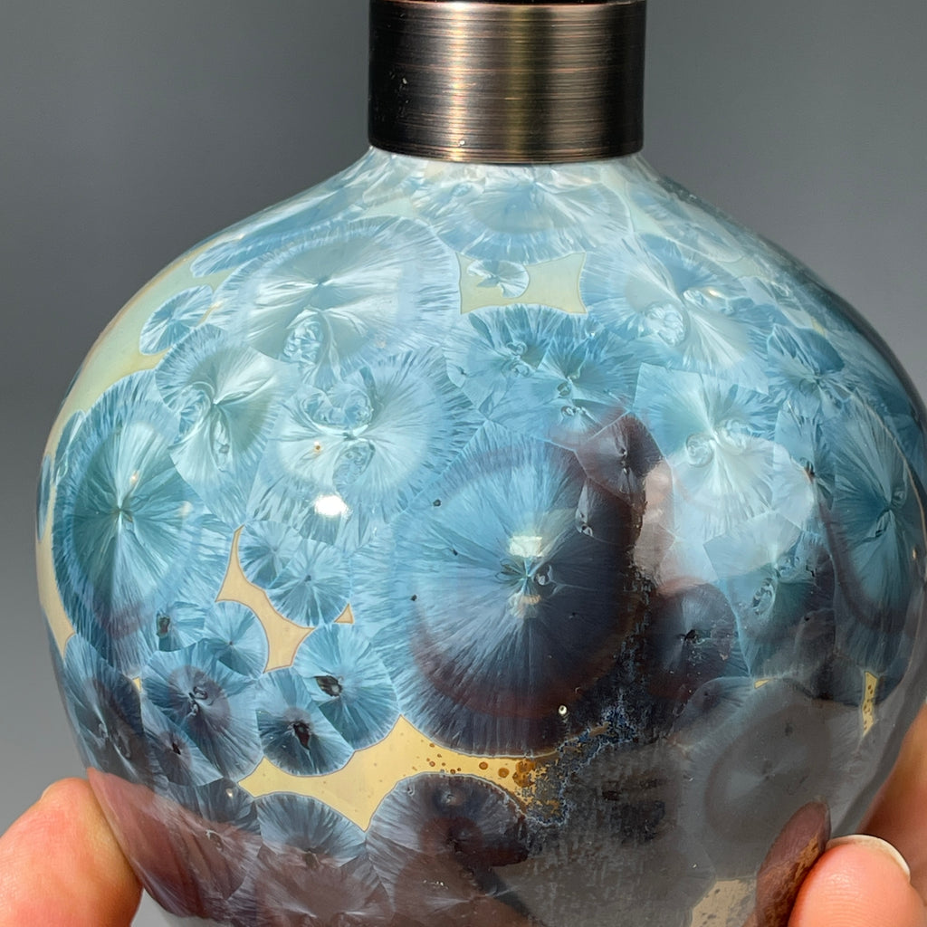 A close-up of a decorative ceramic soap pump featuring a light blue teal and maroon charcoal crystalline glaze