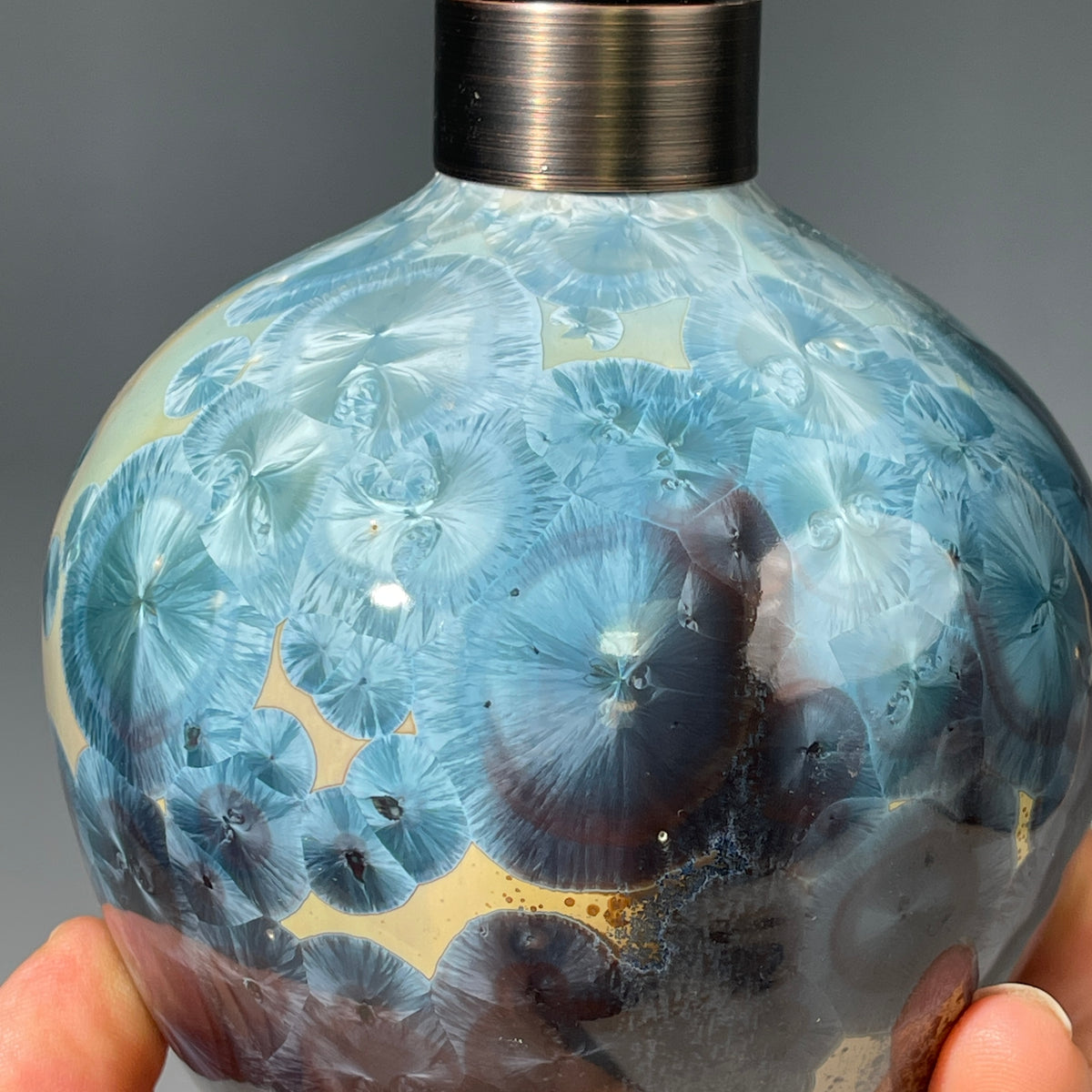 A close-up of a decorative ceramic soap pump featuring a light blue teal and maroon charcoal crystalline glaze