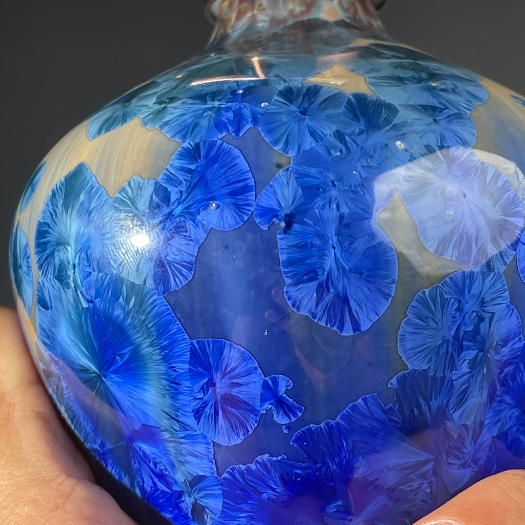 A close up of a  decorative handmade ceramic functional soap dispenser bottle with a glossy blue and gold crystalline pattern, featuring a copper-finished pump dispenser