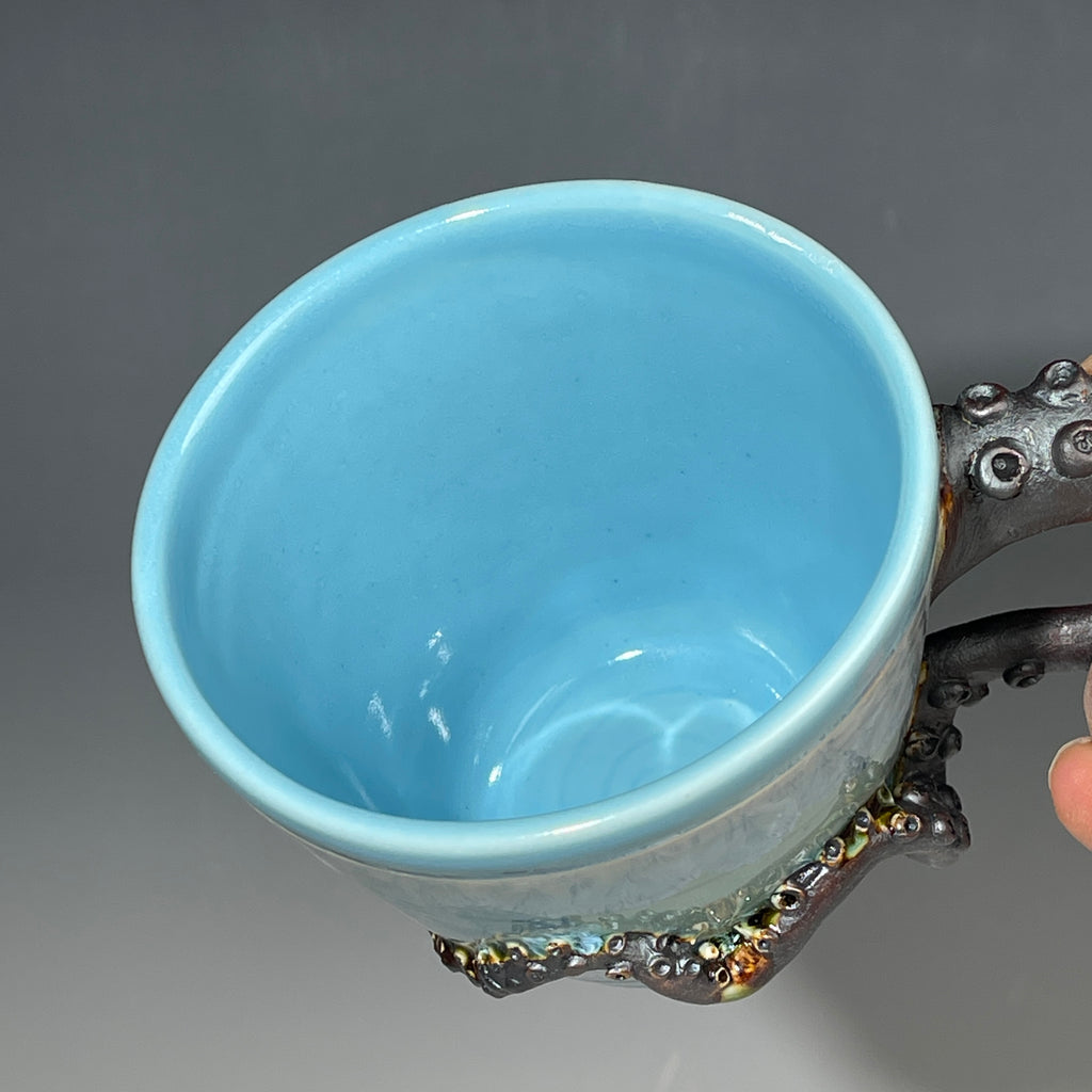 Blue ceramic mug with an octopus handle on a gray background