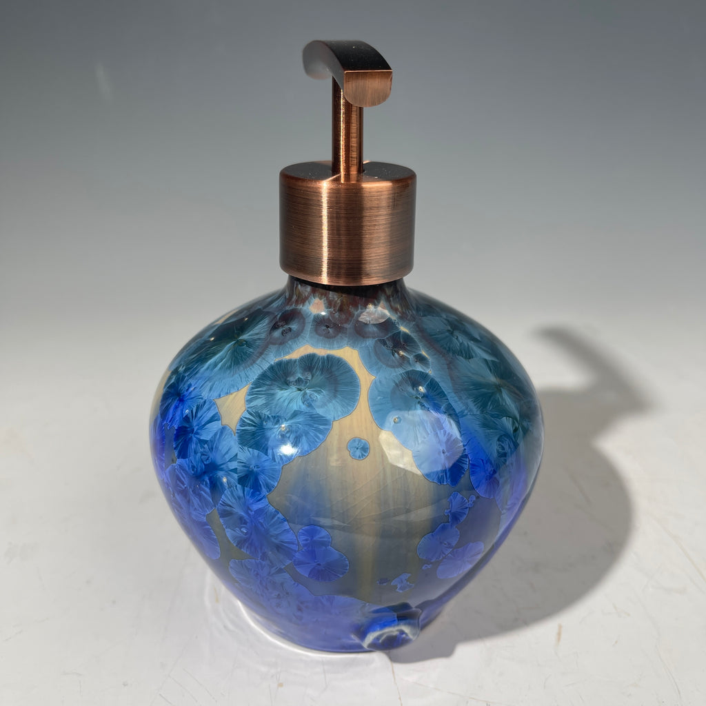 A decorative handmade ceramic functional soap dispenser bottle with a glossy blue and gold crystalline pattern, featuring a copper-finished pump dispenser