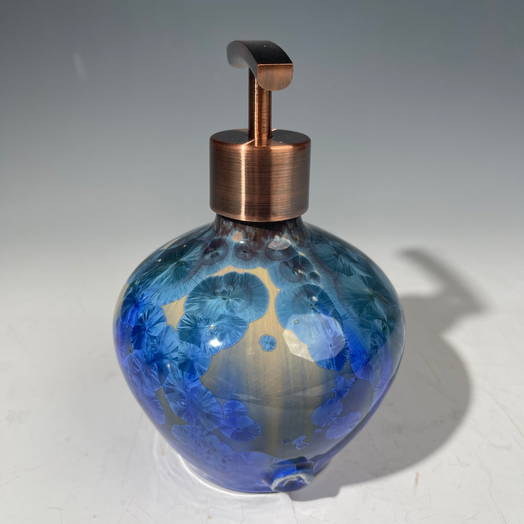 A decorative handmade ceramic functional soap dispenser bottle with a glossy blue and gold crystalline pattern, featuring a copper-finished pump dispenser