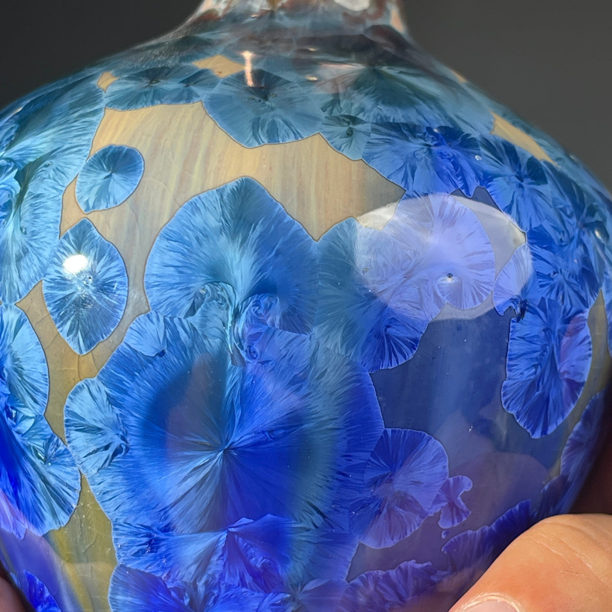 A close up of a  decorative handmade ceramic functional soap dispenser bottle with a glossy blue and gold crystalline pattern, featuring a copper-finished pump dispenser