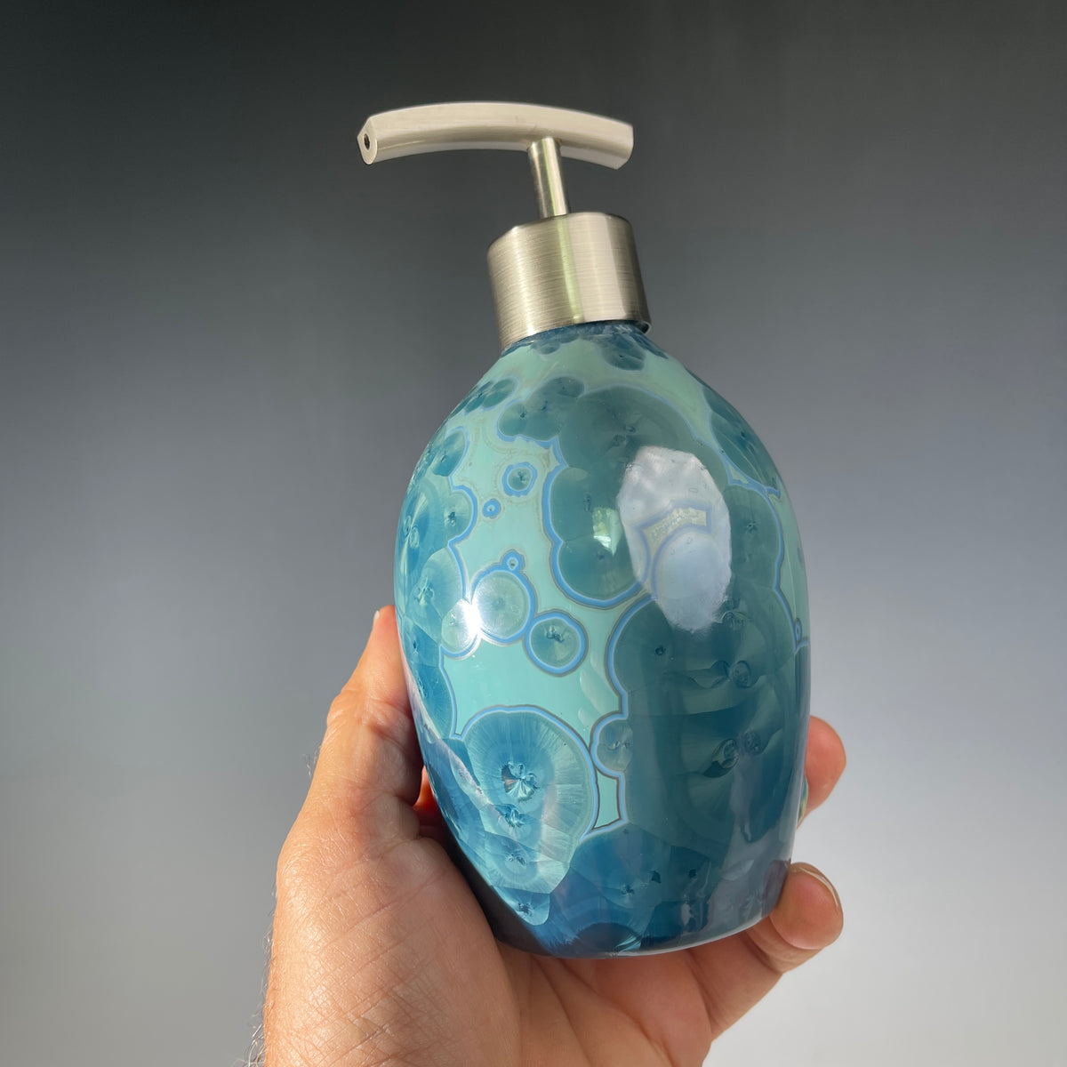close up of a unique art soap dispenser by Hong Rubinstein in an ocean hued sparkling refractive  macro crystalline glaze