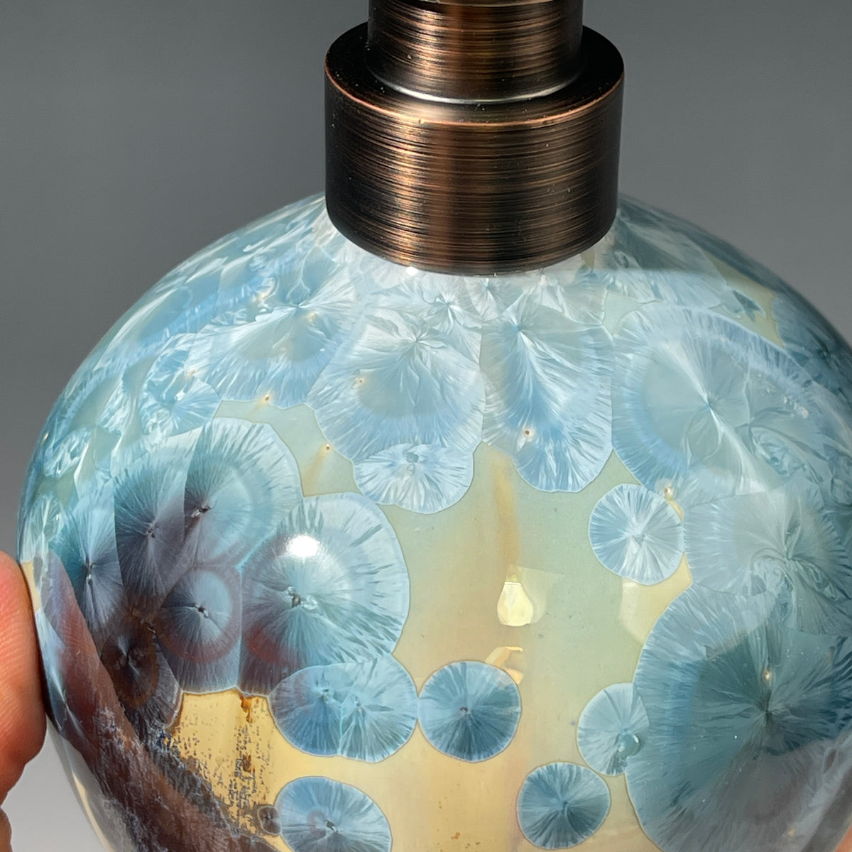 A close-up of a decorative ceramic soap pump featuring a light blue teal and maroon charcoal crystalline glaze