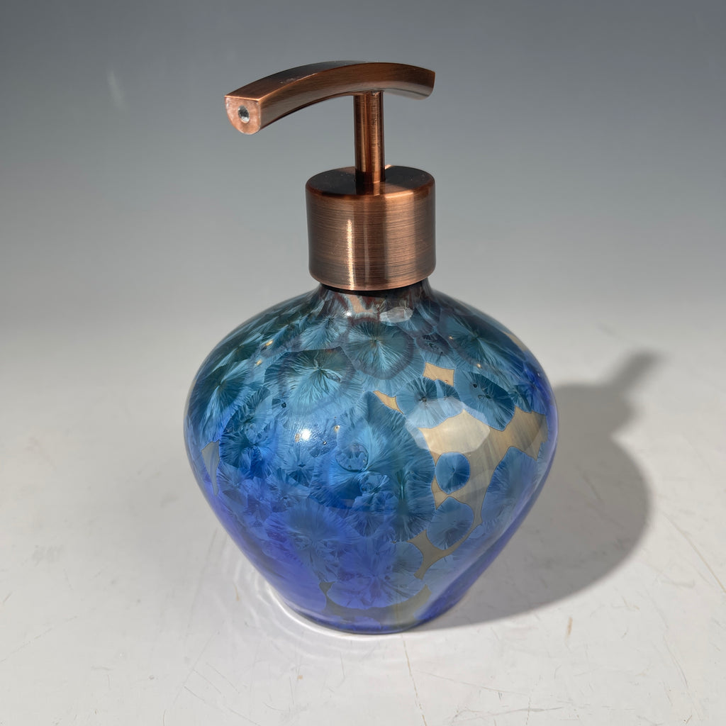 A decorative handmade ceramic functional soap dispenser bottle with a glossy blue and gold crystalline pattern, featuring a copper-finished pump dispenser