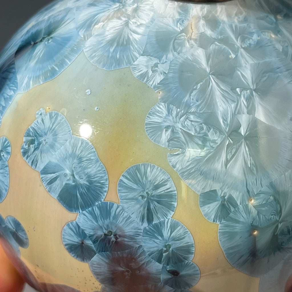 A close-up of a decorative ceramic soap pump featuring a light blue teal and maroon charcoal crystalline glaze