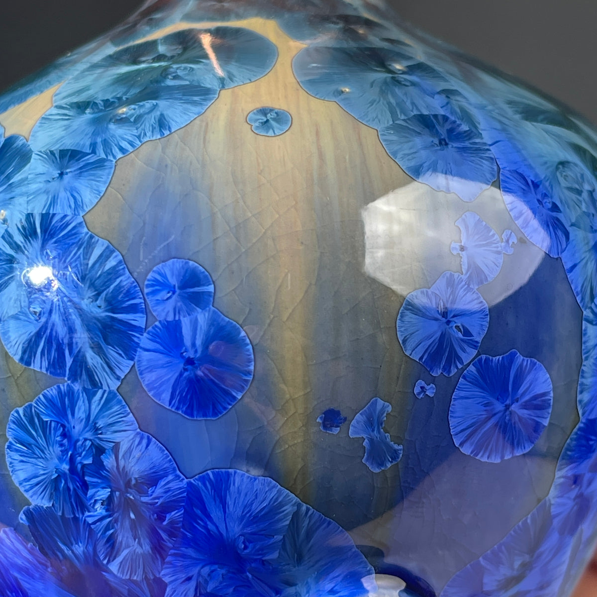 A close up of a  decorative handmade ceramic functional soap dispenser bottle with a glossy blue and gold crystalline pattern, featuring a copper-finished pump dispenser
