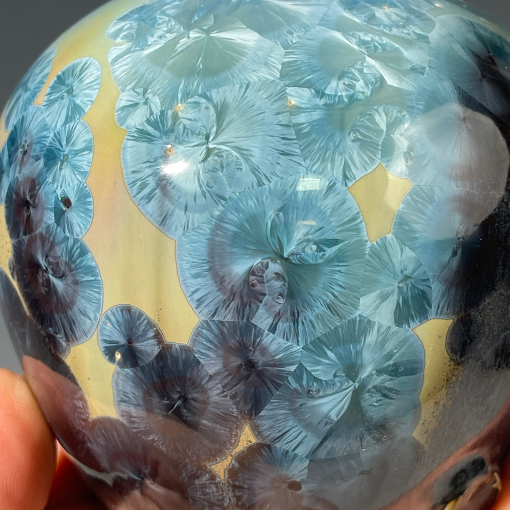 A close-up of a decorative ceramic soap pump featuring a light blue teal and maroon charcoal crystalline glaze