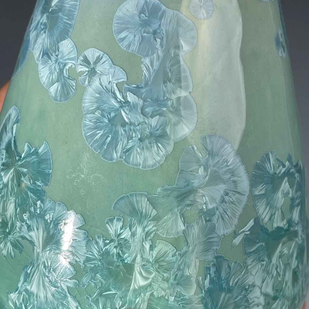  close up of a functional and decorative soap dispenser with a crystalline ceramic  body and a brushed stainless steel pump, shown on a neutral gray background.