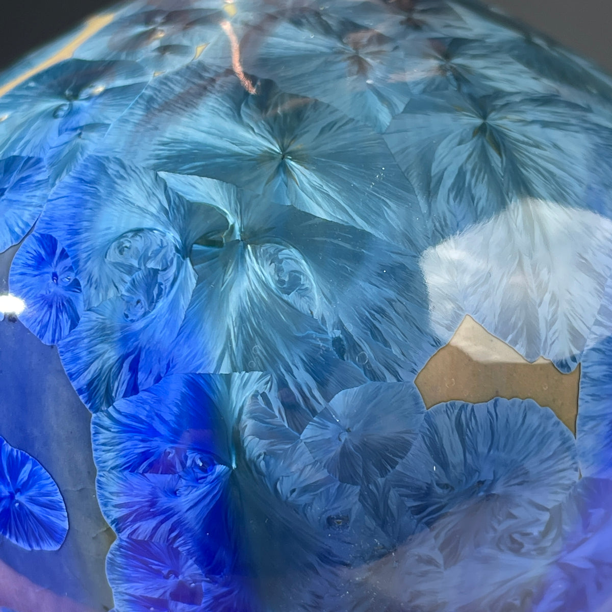 A close up of a  decorative handmade ceramic functional soap dispenser bottle with a glossy blue and gold crystalline pattern, featuring a copper-finished pump dispenser