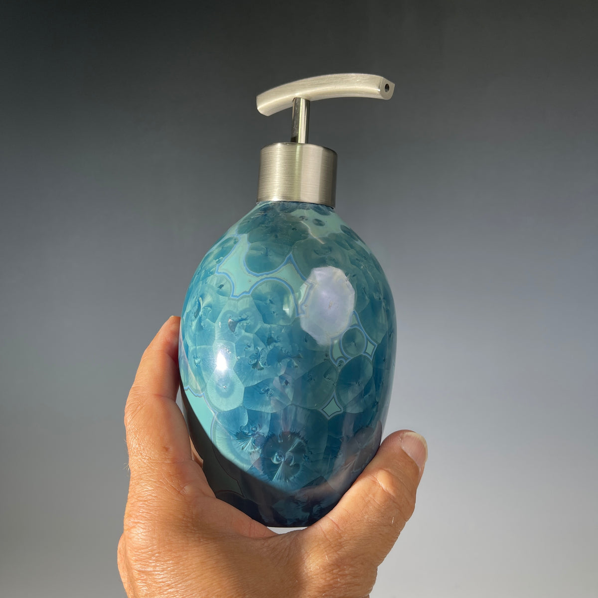 close up of a unique art soap dispenser by Hong Rubinstein in an ocean hued sparkling refractive  macro crystalline glaze