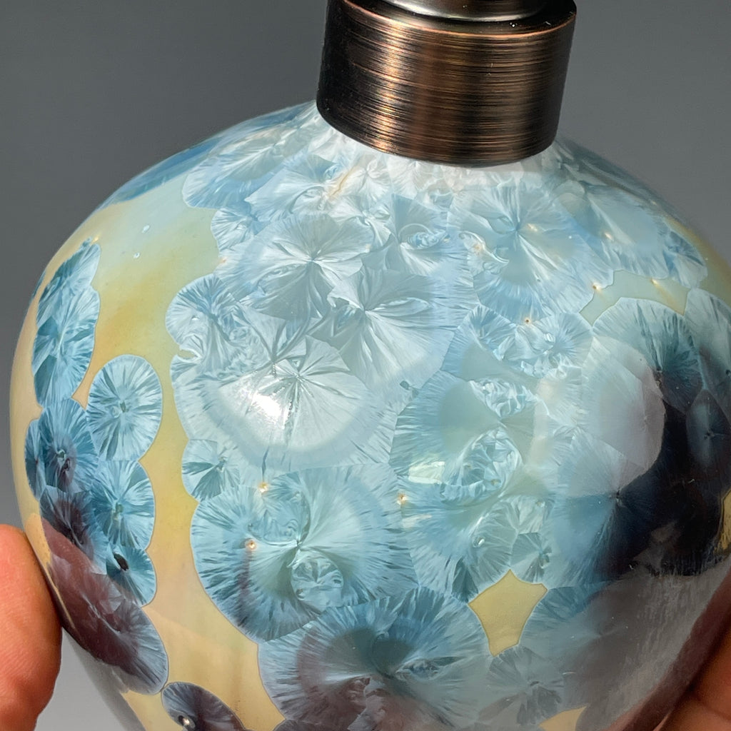 A close-up of a decorative ceramic soap pump featuring a light blue teal and maroon charcoal crystalline glaze