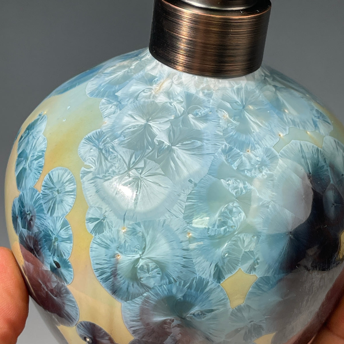 A close-up of a decorative ceramic soap pump featuring a light blue teal and maroon charcoal crystalline glaze