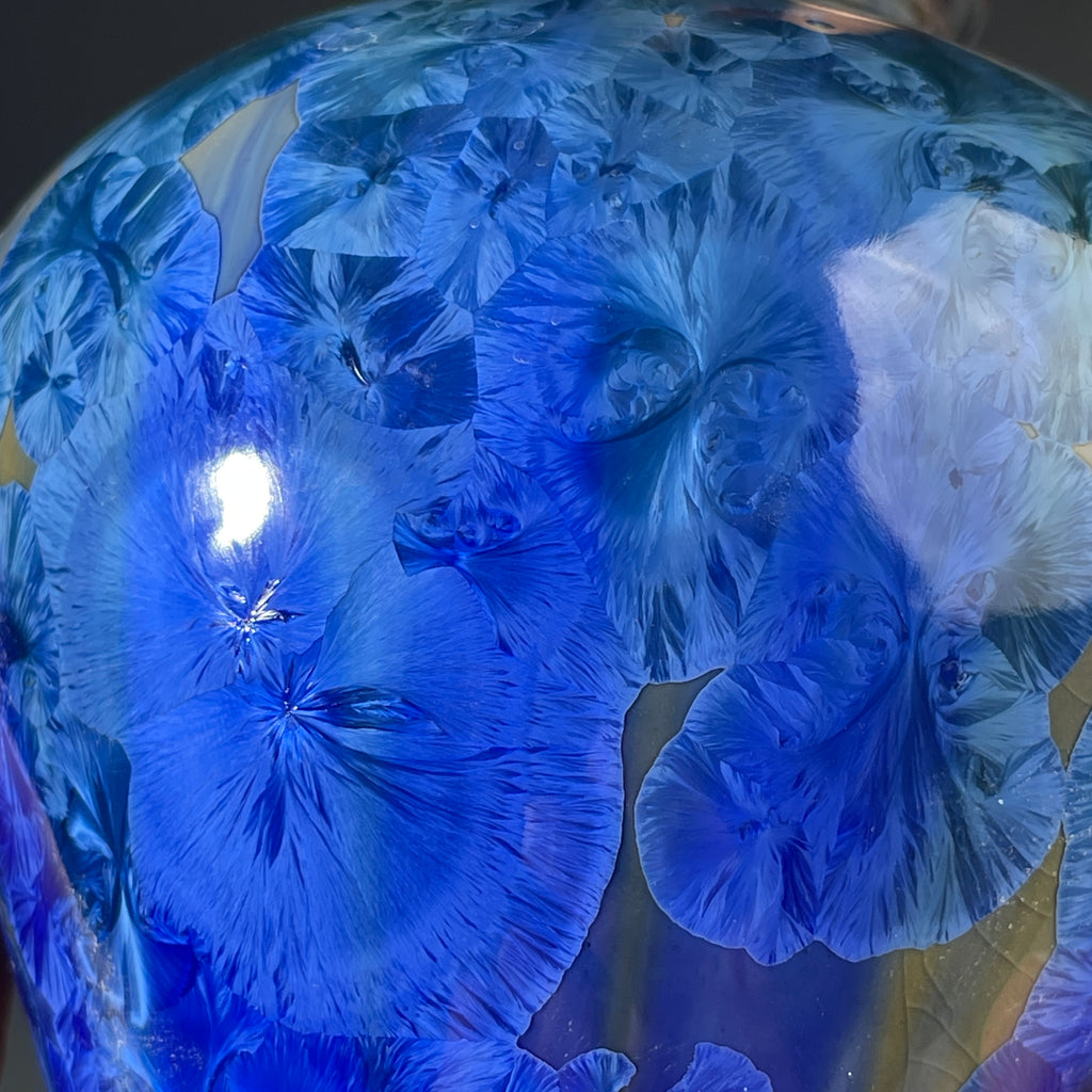 A close up of a  decorative handmade ceramic functional soap dispenser bottle with a glossy blue and gold crystalline pattern, featuring a copper-finished pump dispenser