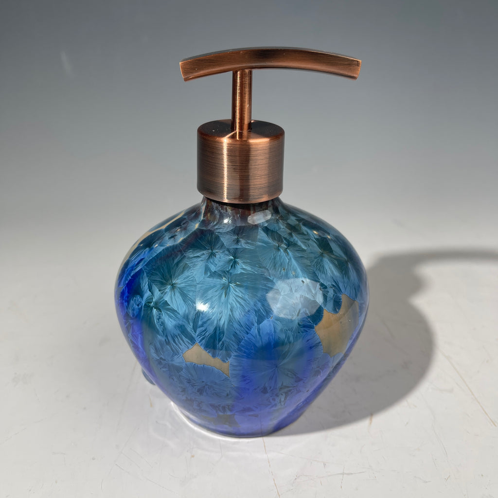 A decorative handmade ceramic functional soap dispenser bottle with a glossy blue and gold crystalline pattern, featuring a copper-finished pump dispenser