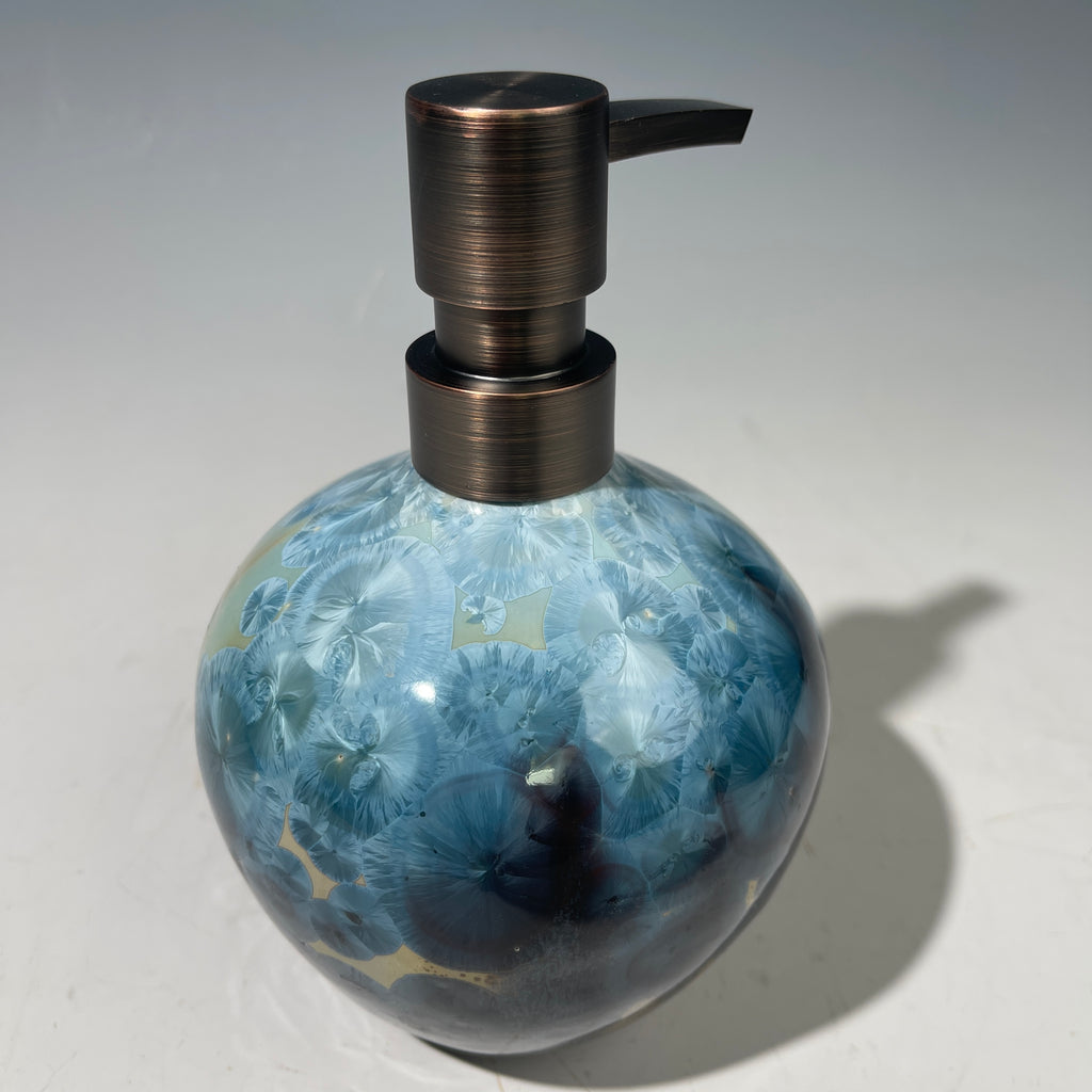A close-up of a decorative ceramic soap pump featuring a light blue teal and maroon charcoal crystalline glaze