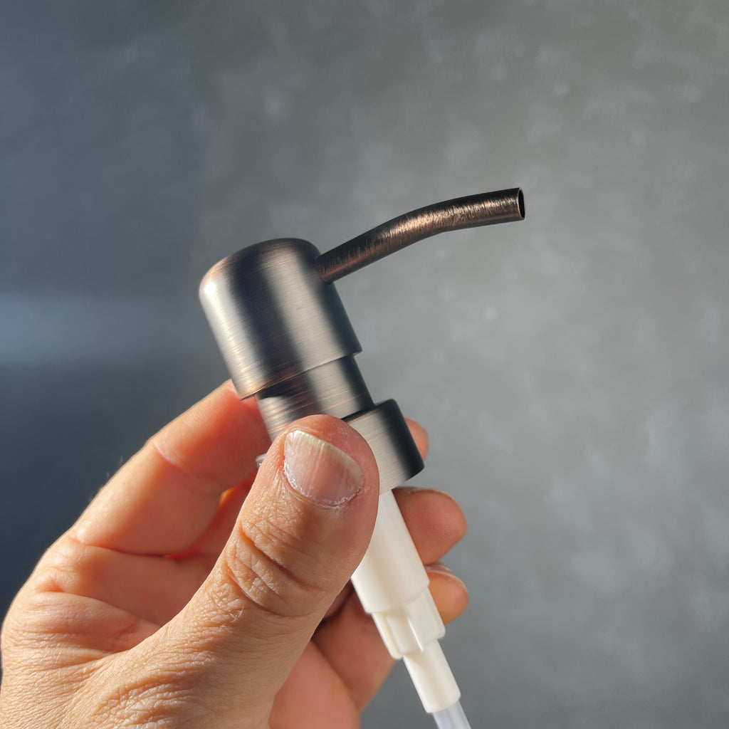 Hand holding a metal oil rubbed bronze soap dispenser with gray background