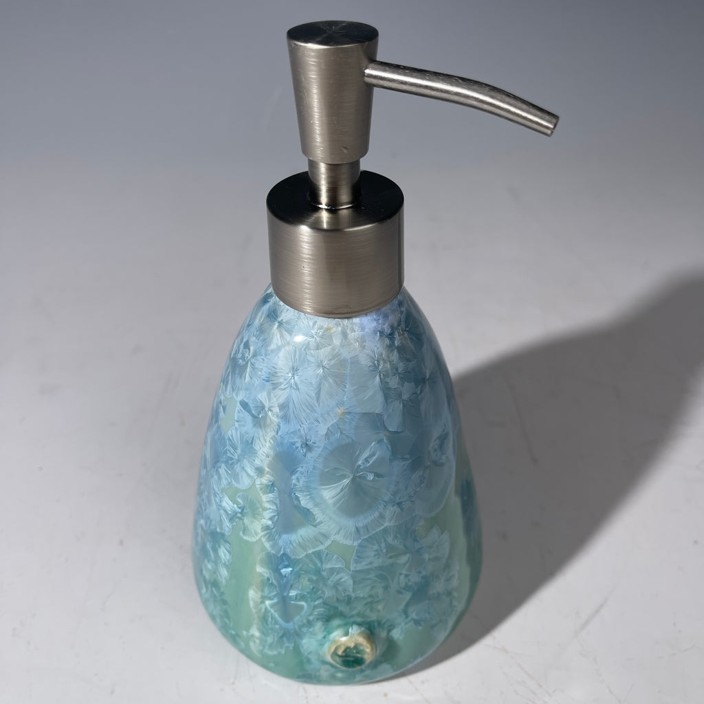 A functional and decorative soap dispenser with a crystalline ceramic  body and a brushed stainless steel pump, shown on a neutral gray background.