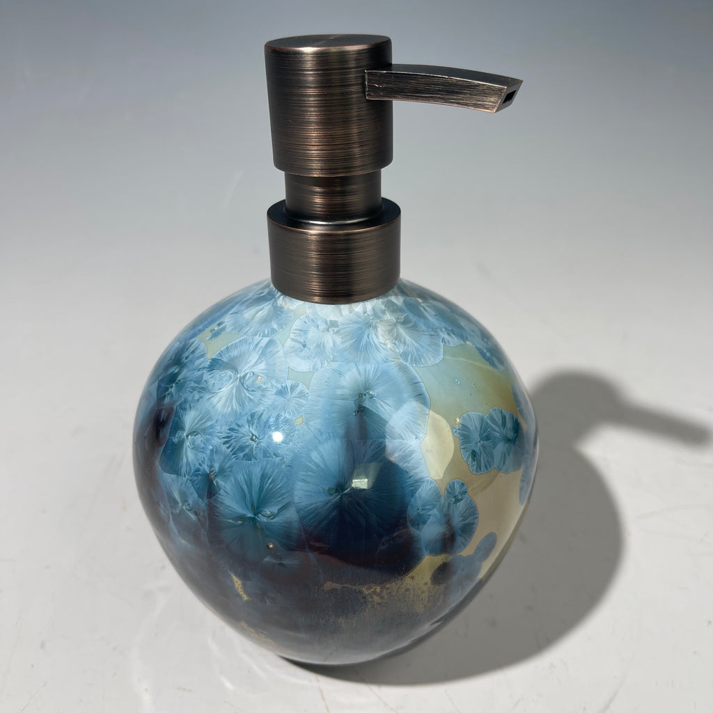 A close-up of a decorative ceramic soap pump featuring a light blue teal and maroon charcoal crystalline glaze