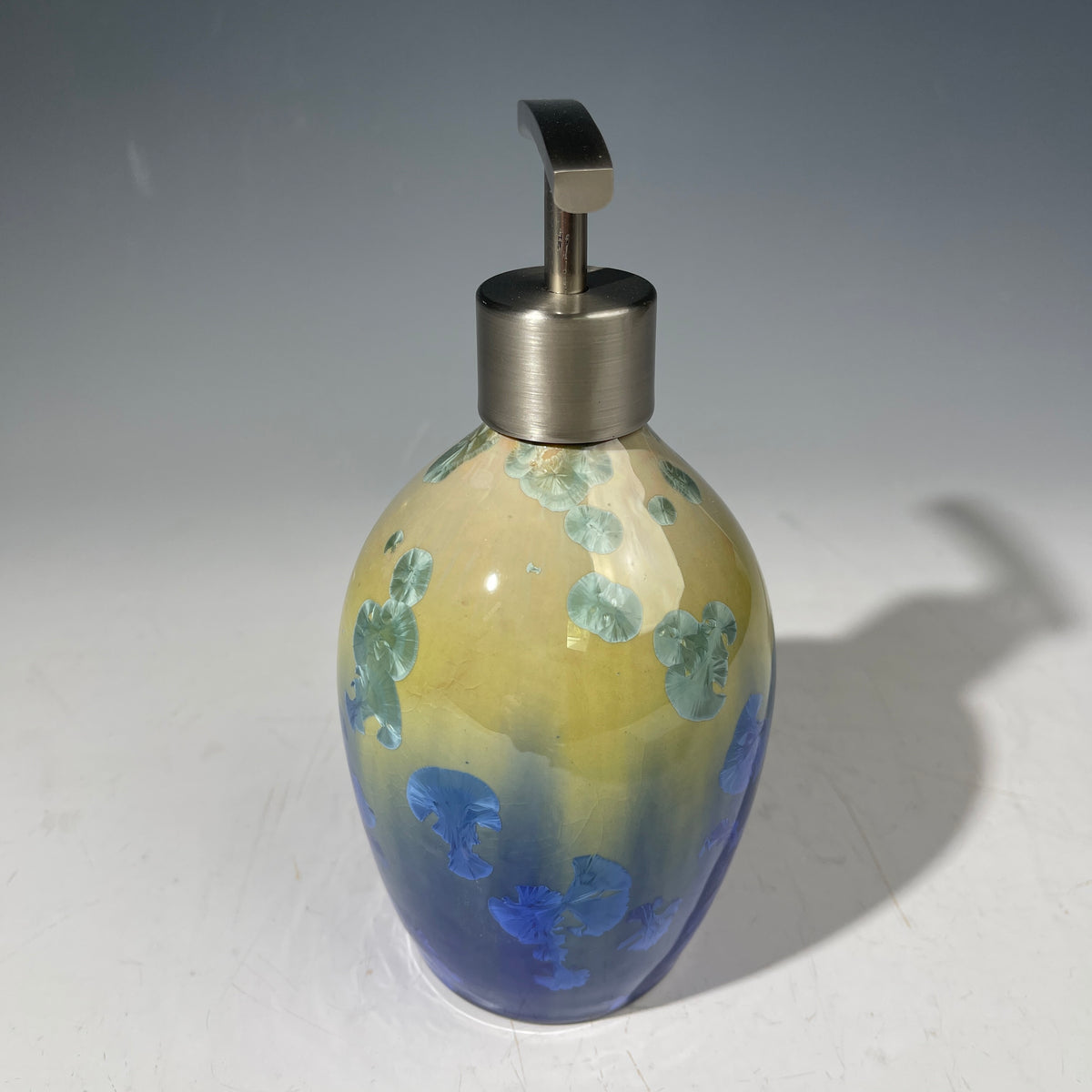  a chartreuse to cobalt crystalline glazed soap dispenser against a gradient background