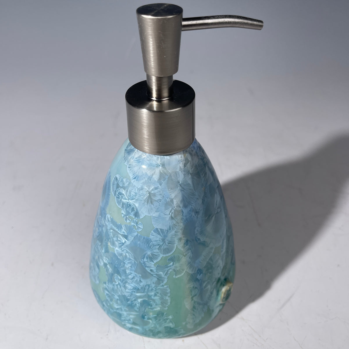 A decorative soap dispenser with a crystalline ceramic  body and a brushed stainless steel pump, shown on a neutral gray background.